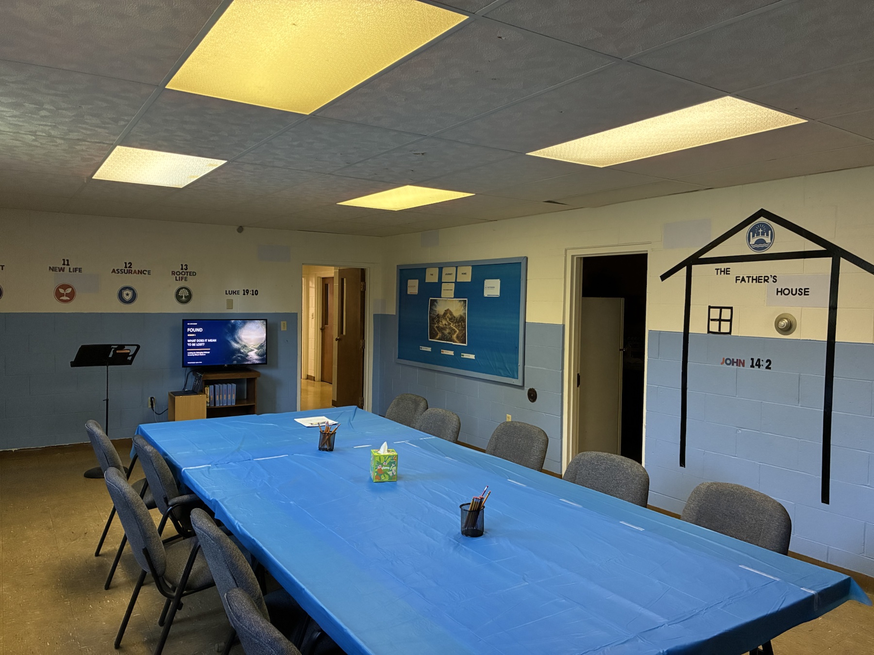 The Found Youth Room prepared for class, with a blue-covered table, lesson screen, journey markers, and the Father's House